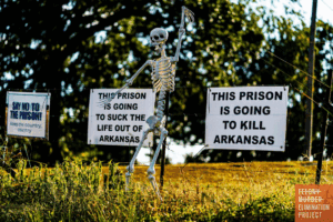 Protest signs (This prison is going to suck the life out of Arkansas; This prison is going to kill Arkansas) near the site of Arkansas’ next prison. (Photo: Bill Gorman/Bolts Magazine)